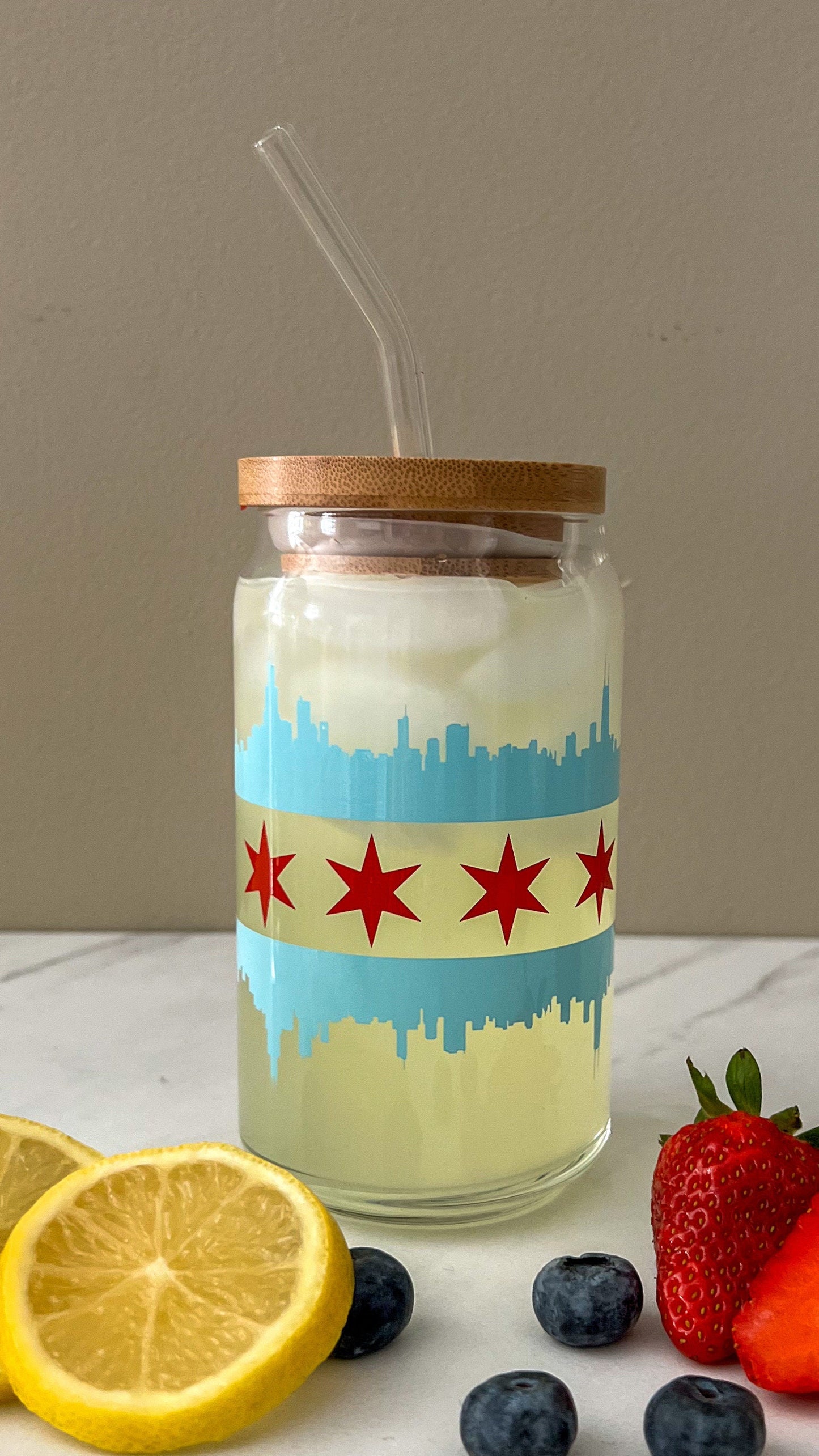 Glass jar with a Chicago flag with the blue skyline and red stars design, wooden lid, and straw on a table with fruit.