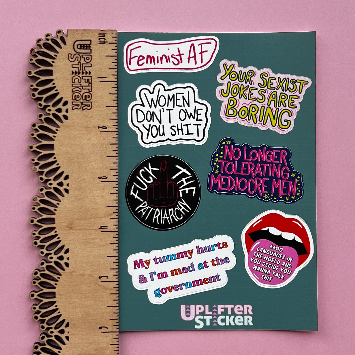 Sticker pack with various statements on a pink background, next to a ruler for size reference.