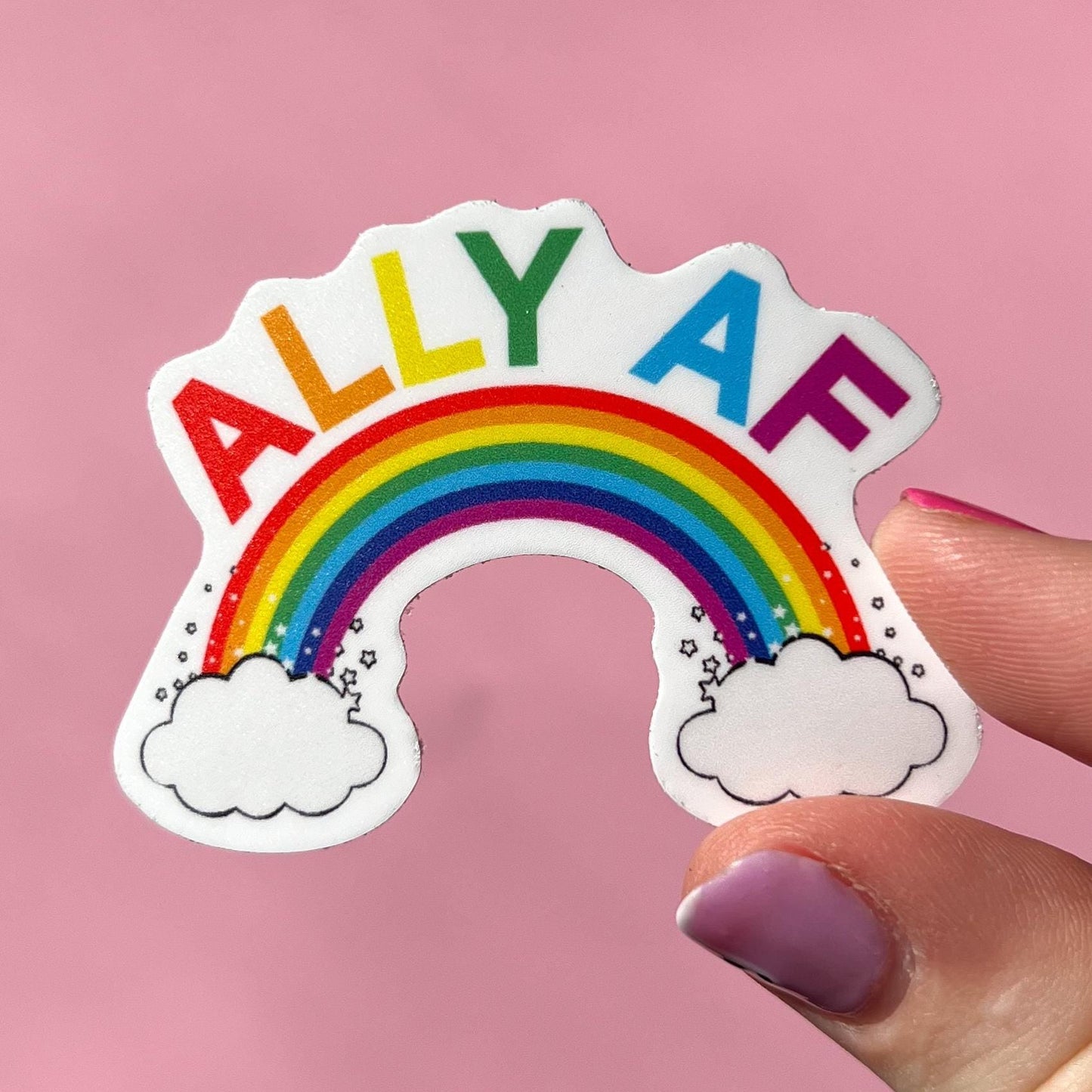 Sticker with rainbow and 'ALLY AF' text held by a hand on a pink background