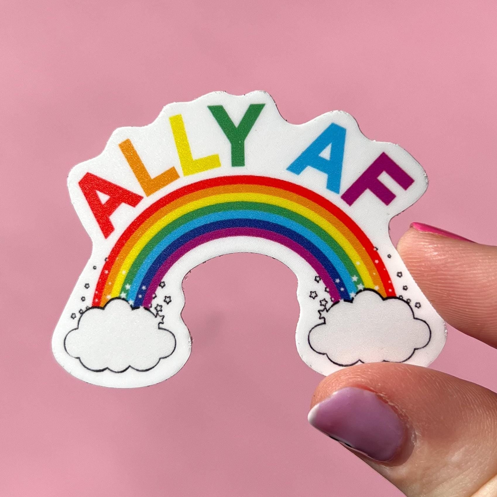 Sticker with rainbow and 'ALLY AF' text held by a hand on a pink background