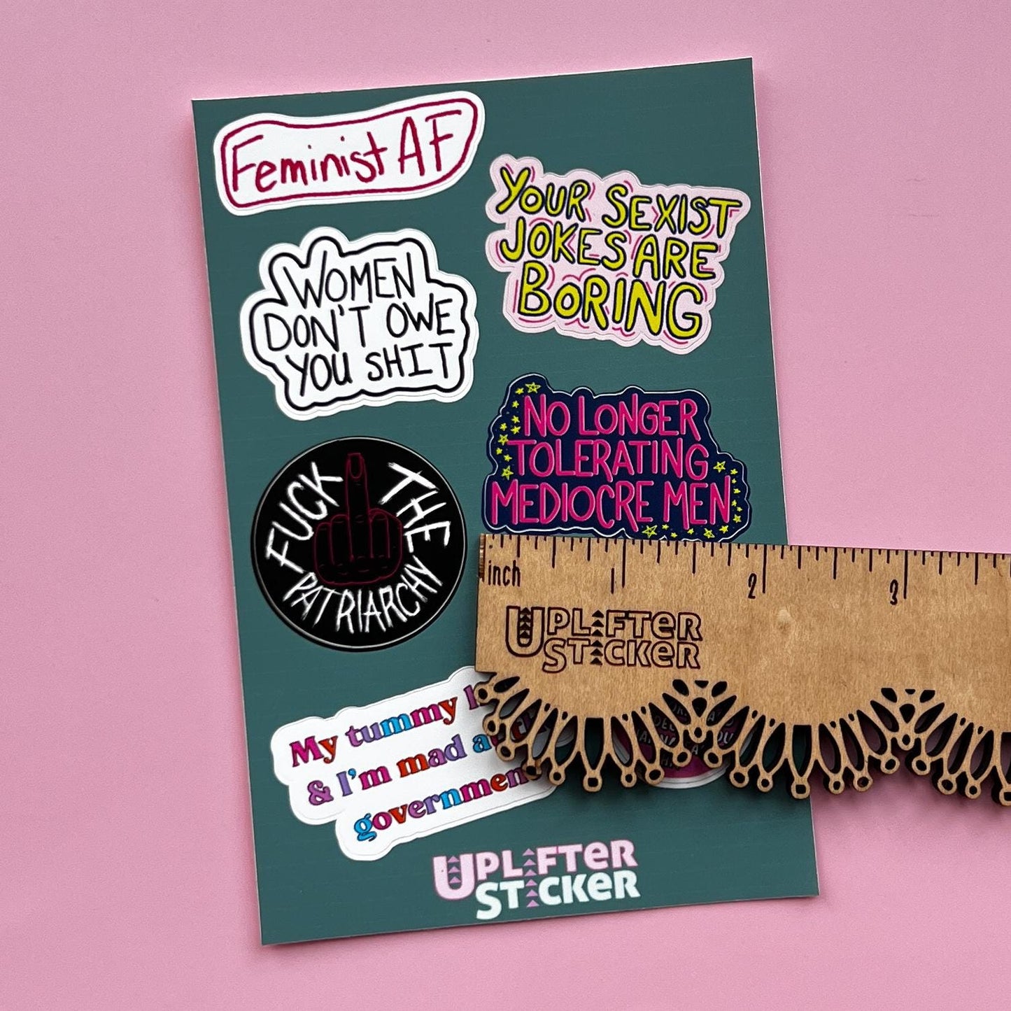 Sticker pack with various statements on a pink background, next to a ruler for size reference.