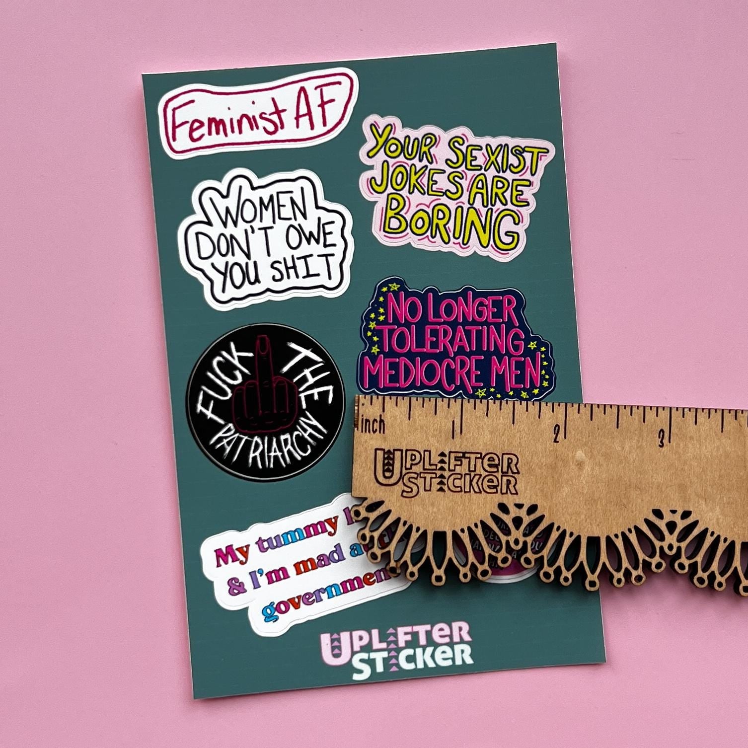Sticker pack with various statements on a pink background, next to a ruler for size reference.