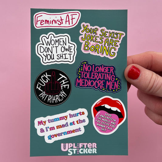 Collection of feminist-themed stickers on a teal card held by a hand with red nail polish.