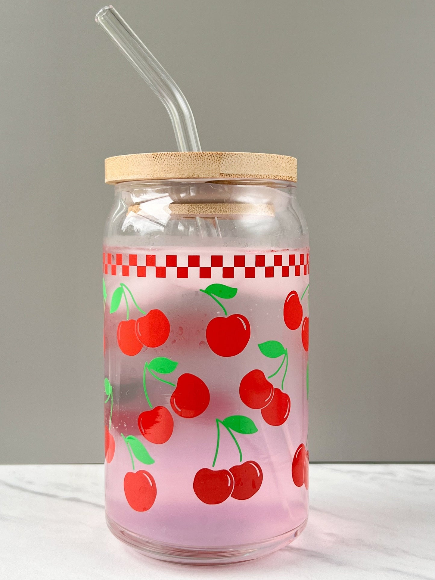 Glass jar with cherry pattern, wooden lid, and straw on a white surface.