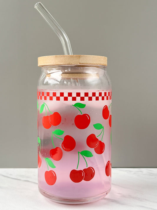 Glass jar with cherry pattern, wooden lid, and straw on a white surface.