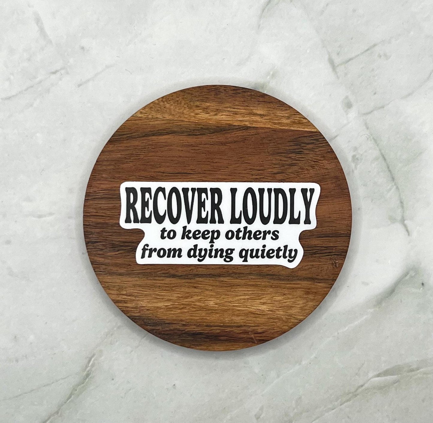 Wooden coaster with Sticker with text 'RECOVER LOUDLY to keep others from dying quietly' on  marble background