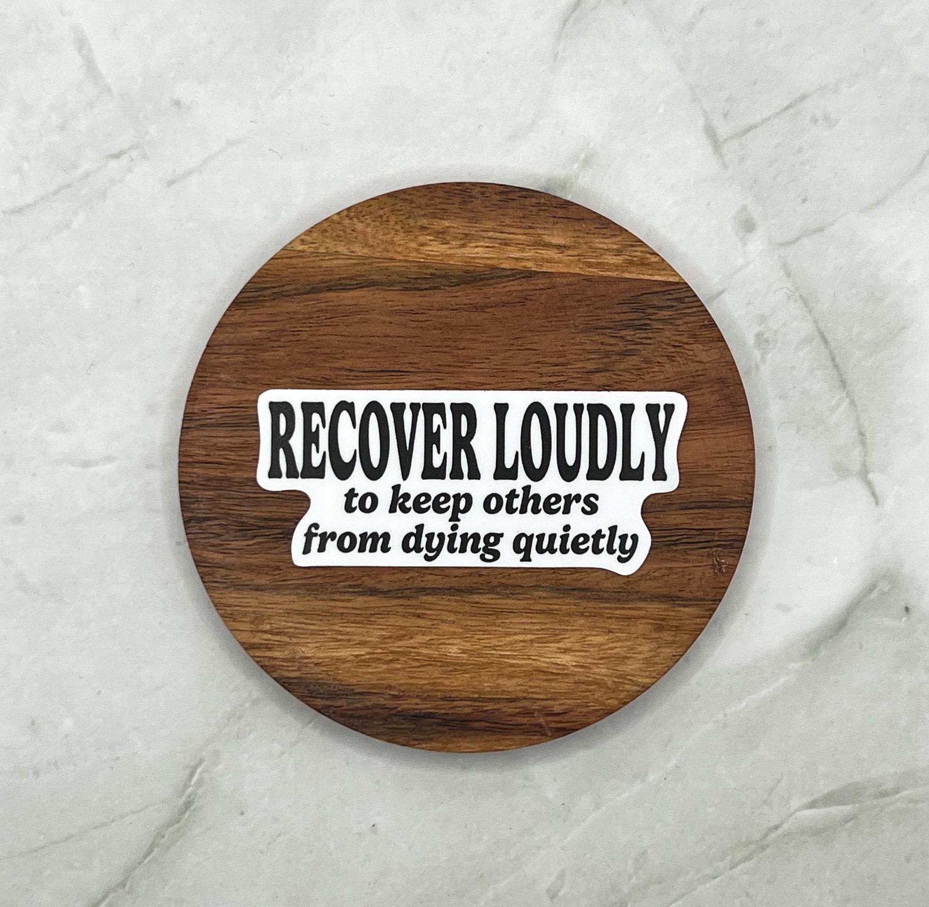Wooden coaster with Sticker with text 'RECOVER LOUDLY to keep others from dying quietly' on  marble background