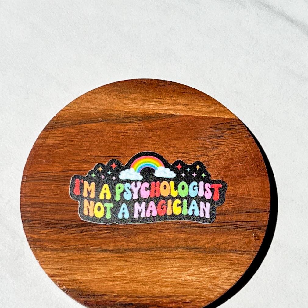 Wooden coaster with a colorful sticker reading 'I'm a psychologist not a magician' on a white background