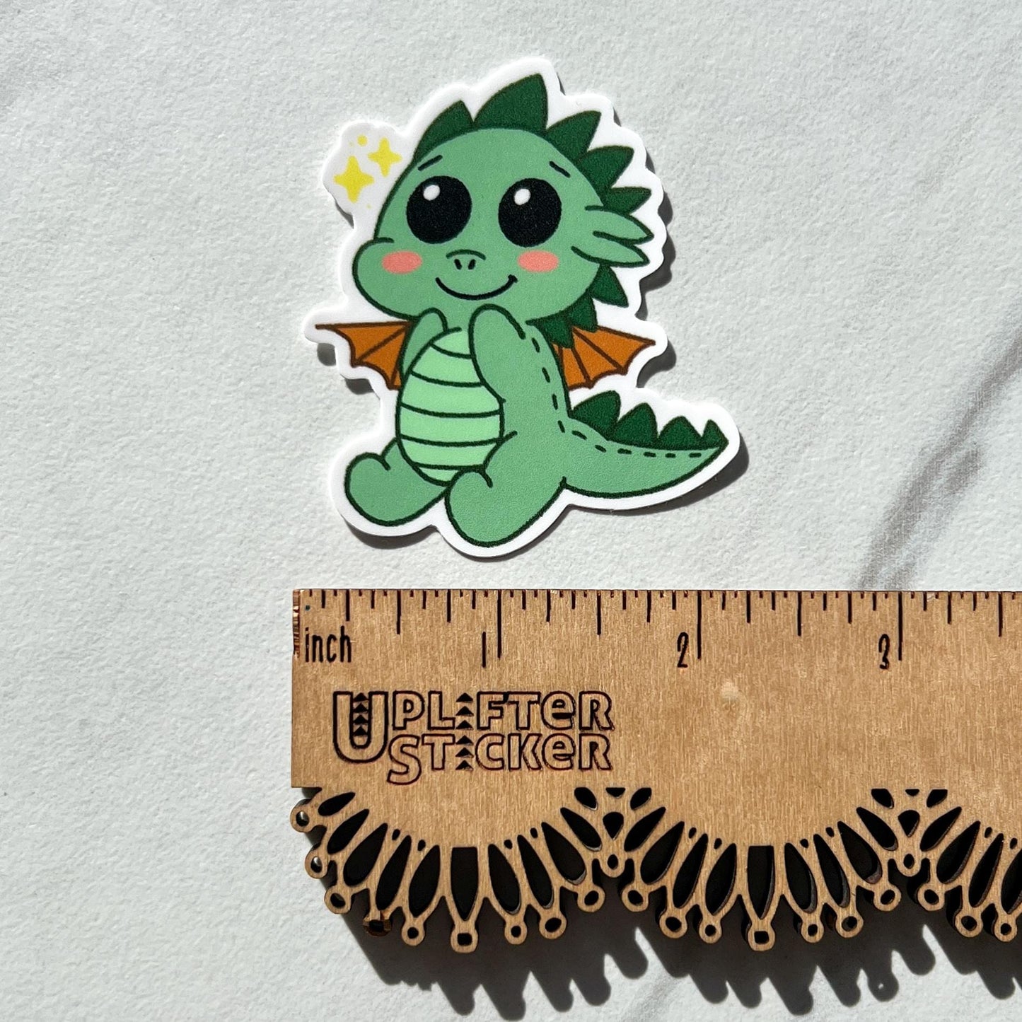 Cartoon dragon sticker next to a ruler on a light gray background